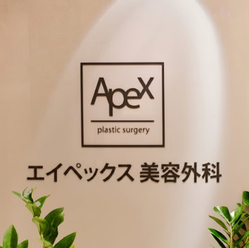 照明に照らされた院内壁面に設置されたエイペックス美容形成外科の英語および韓国語サイン看板ロゴ