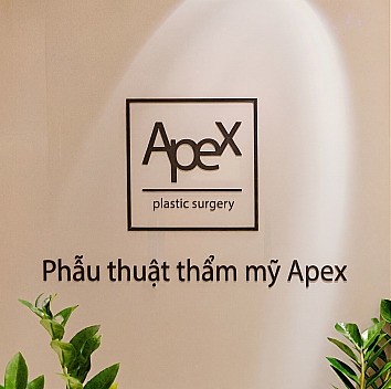 Logo bảng hiệu tiếng Anh và tiếng Hàn của Thẩm mỹ viện APEX gắn trên tường bên trong phòng khám dưới ánh đèn chiếu