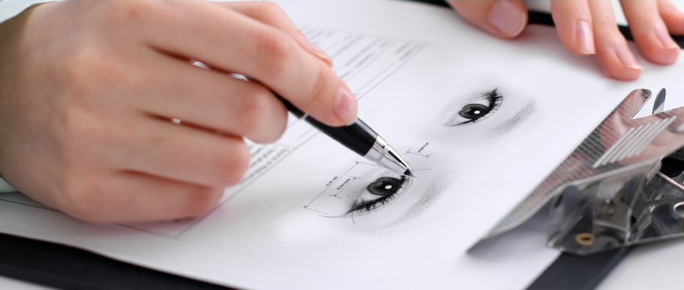 يد تصمم خط الجفن بالقلم على مخطط يحتوي على رسم للعين وقياساتها لاستشارة عملية الجفن المزدوج