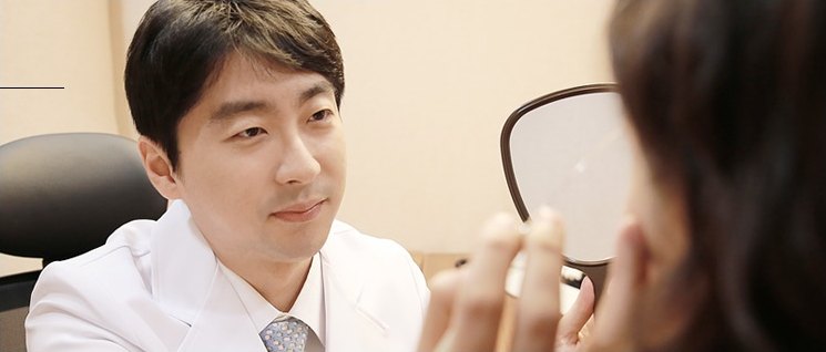 에이펙스성형외과 진료실에서 의사가 손거울을 든 환자와 마주 앉아 성형 상담을 진행하는 모습