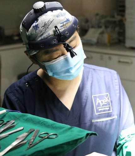 남자 눈성형을 위해 헤드램프와 마스크를 착용하고 소독포 위 수술기구를 내려다보는 에이펙스성형외과 집도의