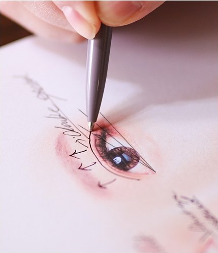종이에 스케치된 눈 그림 위에 펜으로 트임성형 디자인 선과 화살표를 정밀하게 제도하는 모습