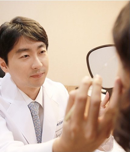 트임성형 상담을 위해 손거울을 들고 있는 환자의 눈매를 진찰하는 에이펙스성형외과 의료진