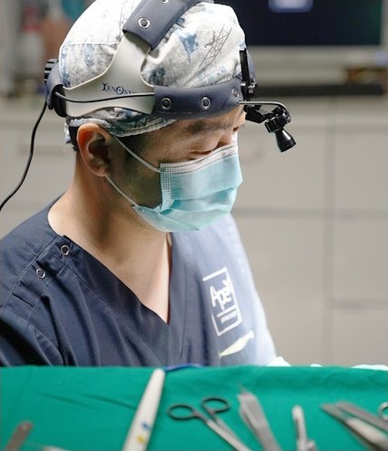 Hình ảnh bác sĩ phẫu thuật đeo đèn đội đầu và kính lúp phóng đại, đeo khẩu trang tập trung phẫu thuật nâng cung mày trên