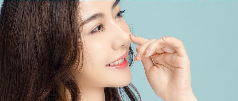 민트색 배경 앞에서 손가락으로 자연스러운 콧대를 가리키며 밝게 미소 짓는 여성의 무보형물 코성형 프로필