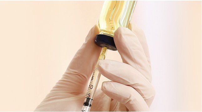 라텍스 장갑을 착용한 손으로 약병에서 물광주사 용액을 주사기로 정밀하게 추출하는 모습