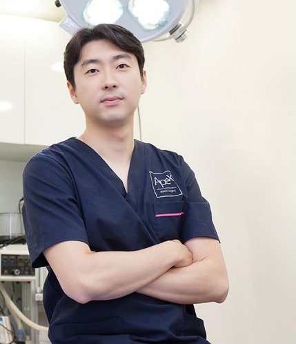 수술실 조명 아래에서 네이비색 수술복을 입고 팔짱을 낀 채 정면을 바라보는 에이펙스성형외과 눈재수술 의료진