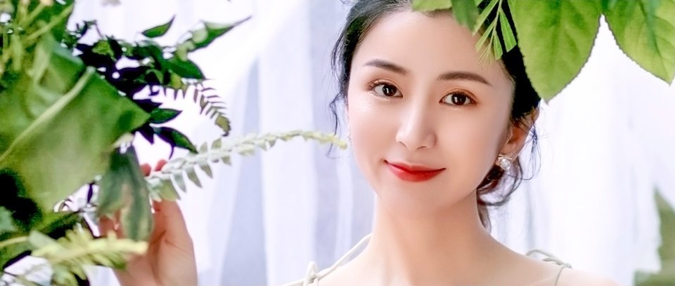 초록 잎사귀 배경 속에서 깨끗하고 탄력 있는 눈가를 드러내며 미소 짓는 여성의 하안검 수술 클로즈업 모습