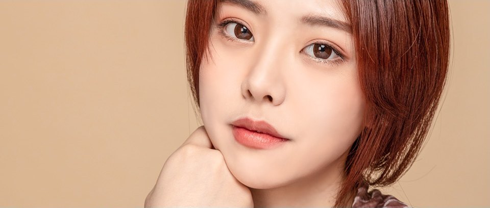 갈색 단발머리의 여성이 턱을 손에 괴고 정면을 응시하는 얼굴지방이식 클로즈업 모델