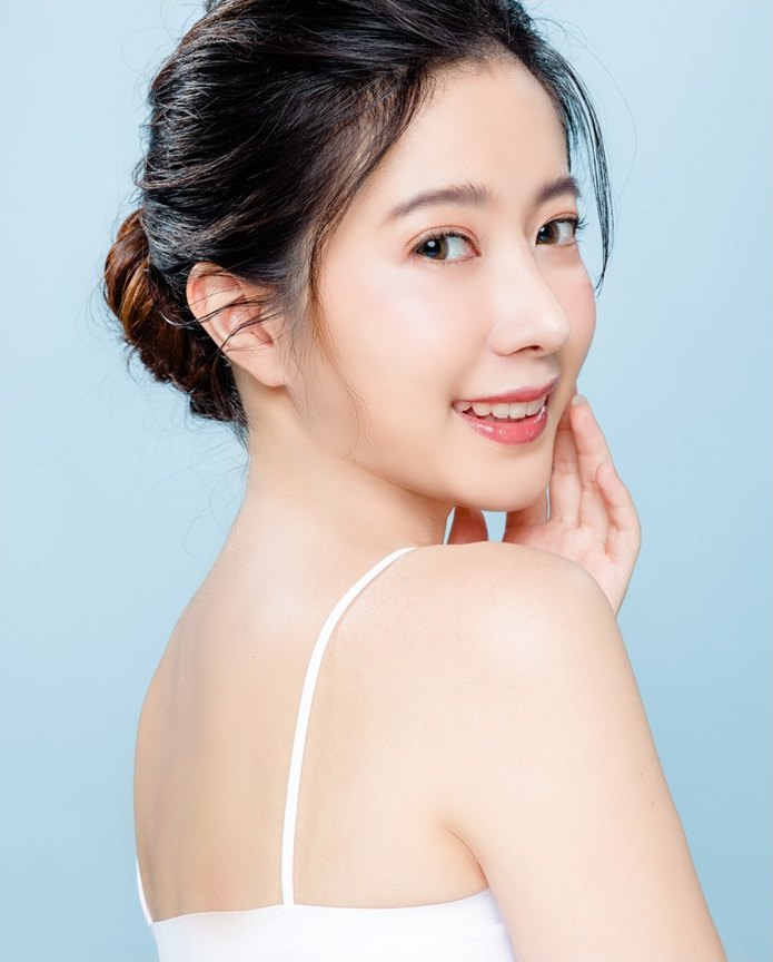 머리를 묶은 여성이 뒤를 돌아보며 미소 짓고 있는 에이펙스성형외과 얼굴지방이식 클로즈업 모델