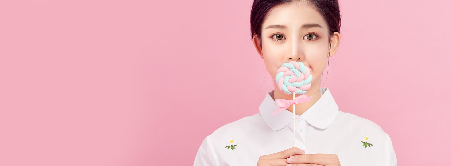 Banner atas operasi hidung pengecilan cuping hidung menampilkan seorang wanita dengan latar belakang merah muda yang menutupi bibirnya dengan permen lolipop