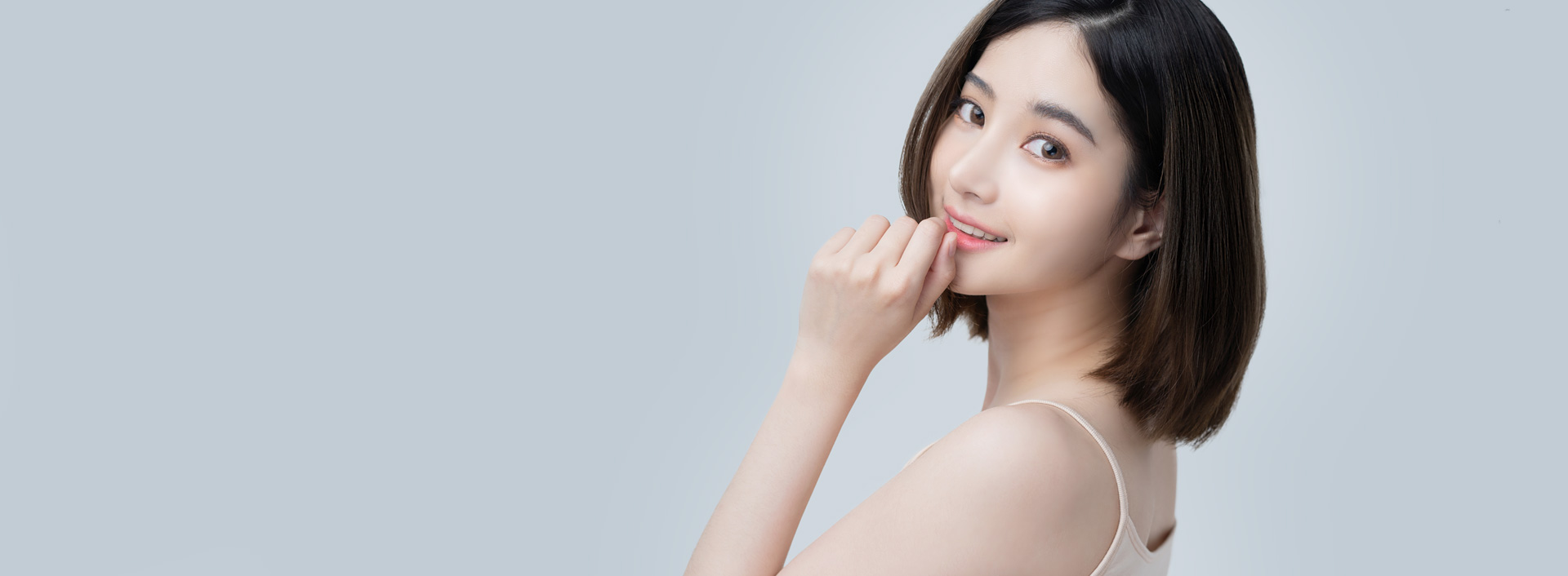 ภาพหญิงสาวผมสั้นเอามือแตะคาง ยิ้มและเหลียวมองกลับมา ในหน้าเกี่ยวกับศัลยกรรมปลายจมูกของ APEX Plastic Surgery